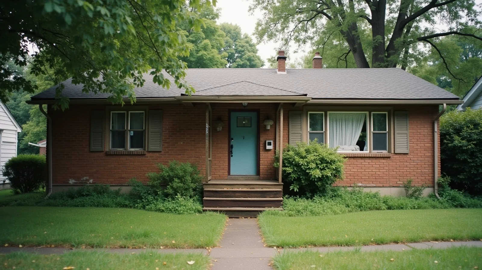 Brick ranch house with peeling trim paint and overgrown yard, shown in as-is condition before sale