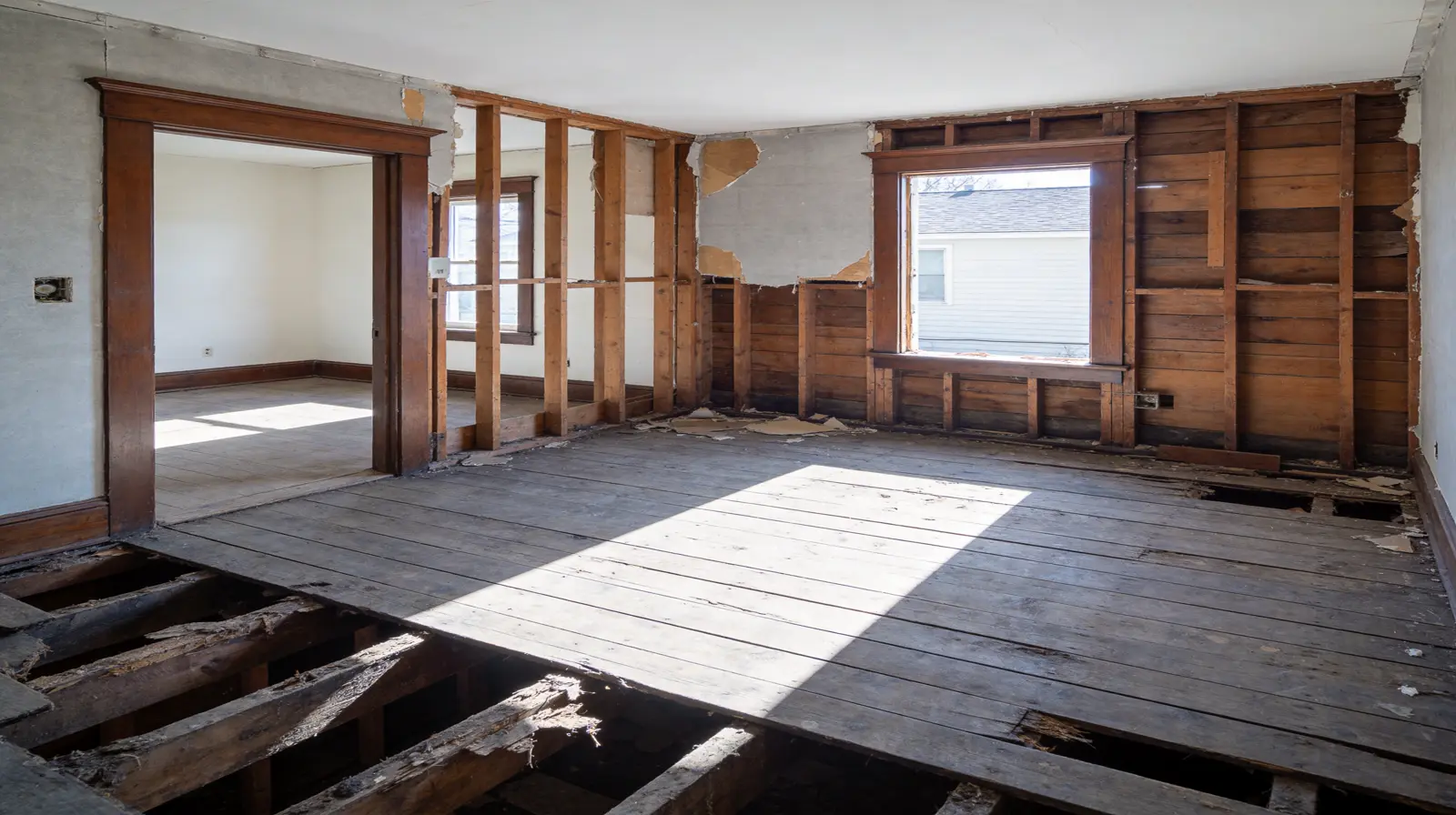 Gutted residential interior showing exposed wood framing, bare studs, and missing plaster walls ready for total renovation